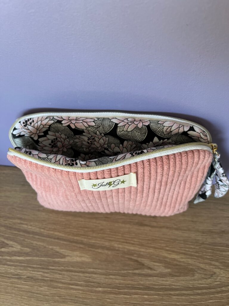 Pochette matelassée rose pastel ouverte montrant sa doublure en tissu floral noir, rose et blanc